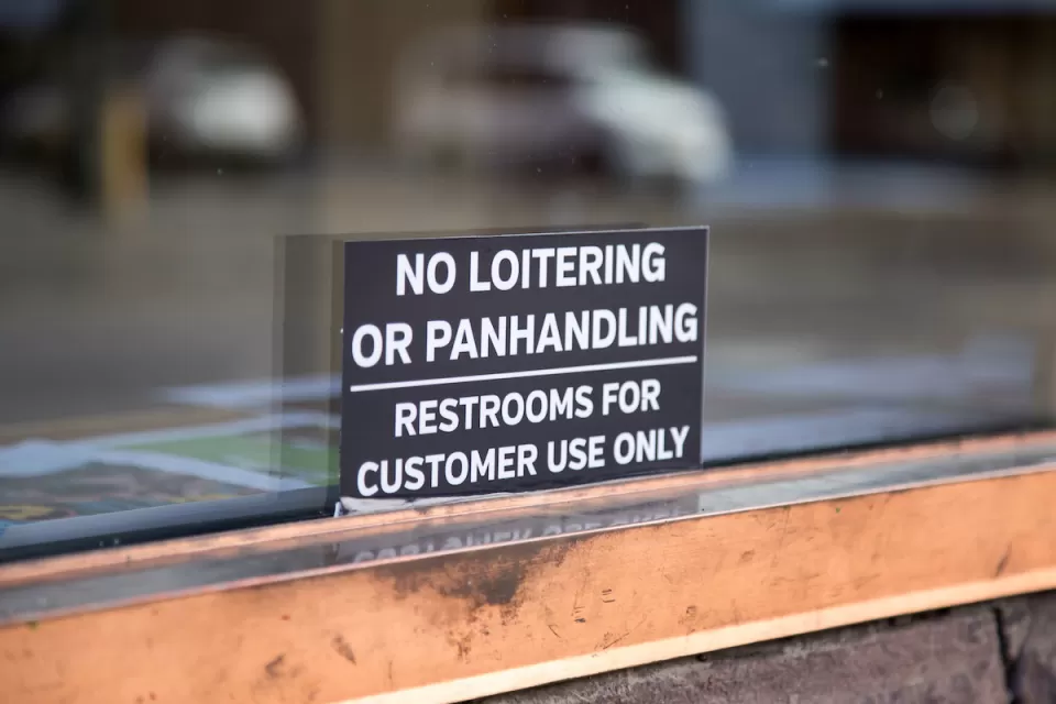 Close-up of "No Loitering or Panhandling - Restrooms for Customer Use Only" sign in shop window.